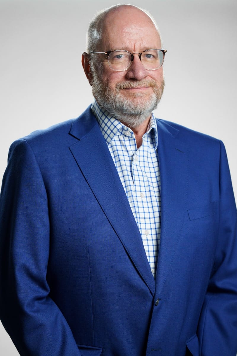 Professional portrait of a company executive in a blue blazer and checkered shirt.